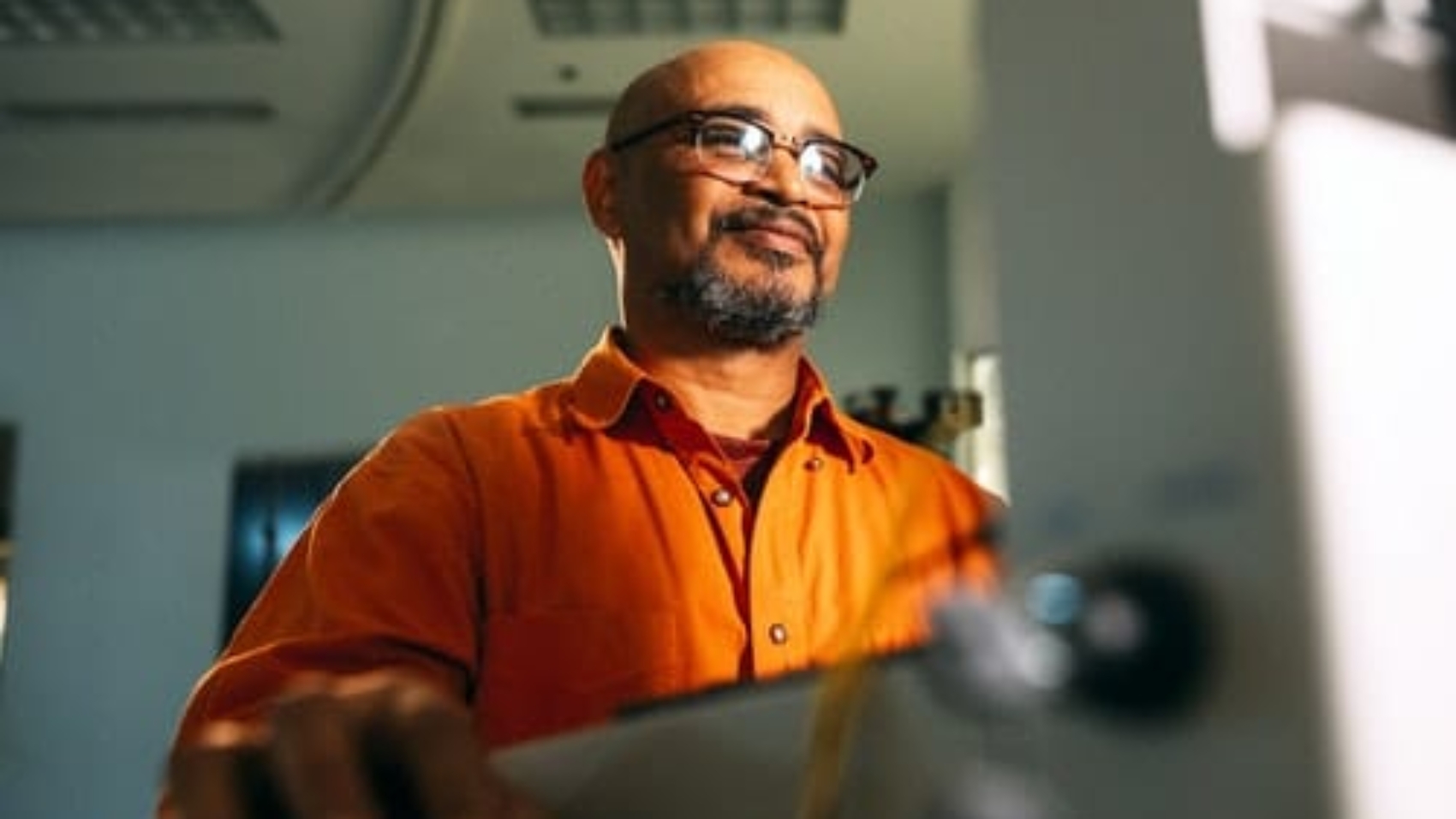 man with glasses wearing orange shirt sitting in front of computer