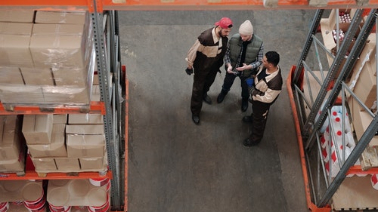 three workers standing and talking between aisles in a warehouse