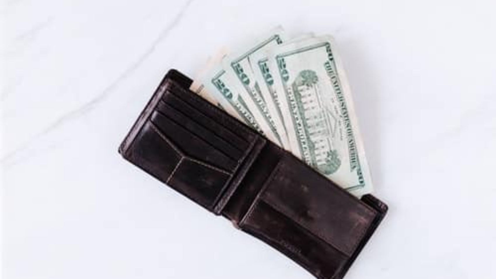 leather wallet sitting on table with four twenty-dollar bills coming out of it