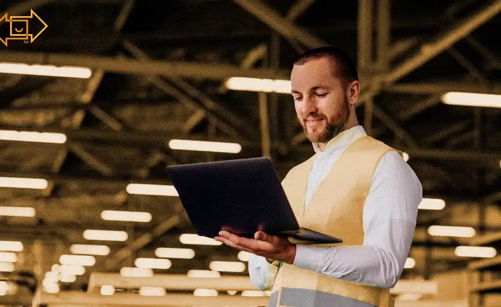 male worker with a safety vest holding laptop in a warehouse