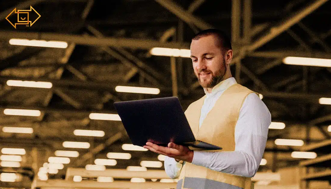male worker with a safety vest holding laptop in a warehouse