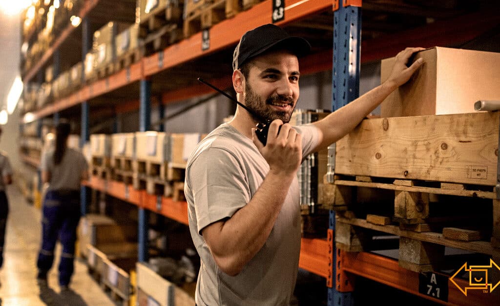 motivated warehouse employee smiling while holding up a walkie talkie