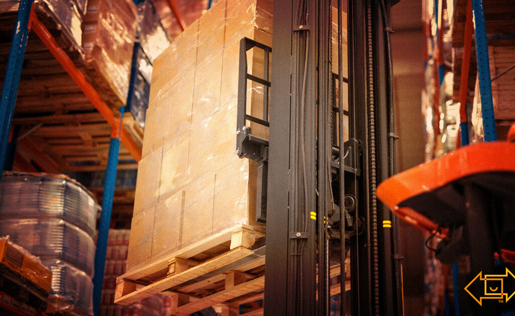 industrial forklift machine lifting palette of cardboard boxes and placing them on shelves in a warehouse